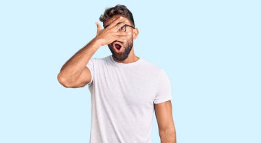 Günlük kıyafetler ve gözlük takan genç İspanyol adam şok içinde yüzünü ve gözlerini kapayarak utangaç ifadesiyle parmaklarından bakıyor.. 