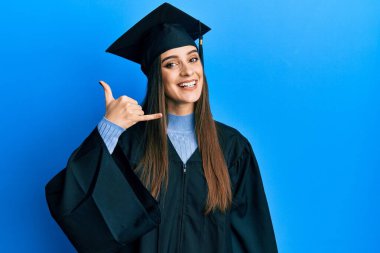 Güzel esmer bir kadın mezuniyet şapkası ve tören cübbesi takıyor gülümsüyor telefonla el ve parmak hareketleri yapıyor telefonda konuşuyor gibi. iletişim kavramları. 