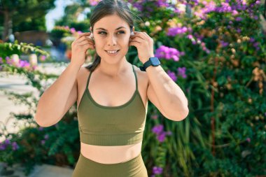 Genç sarışın sporcu parkta kulaklık takarak egzersiz yapıyor.