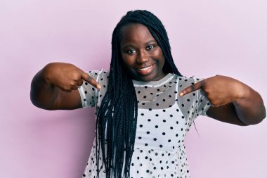 Saçları örgülü genç siyahi bir kadın. Kendine güvenen, güler yüzlü, kendini gururlu ve mutlu gösteren bir kadın.. 