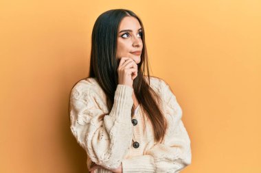 Güzel, esmer, günlük kıyafetler giyen genç bir kadın şüphe üzerine yoğunlaşmış, çenesinde parmak olan ve kafasını kaldırıp merak eden bir kadın. 