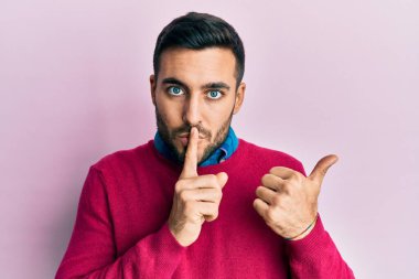 Gündelik giysiler giyen genç İspanyol adam sessiz olmak istiyor. Parmakları dudaklarında, elleri yandan işaret ediyor. sessizlik ve gizli konsept. 