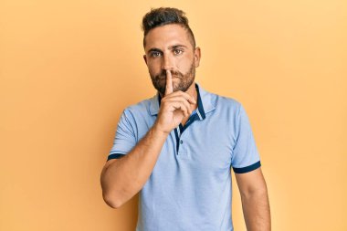 Sakallı, sıradan kıyafetler giyen, dudakları parmaklarıyla sessiz olmak isteyen yakışıklı bir adam. sessizlik ve gizli konsept. 