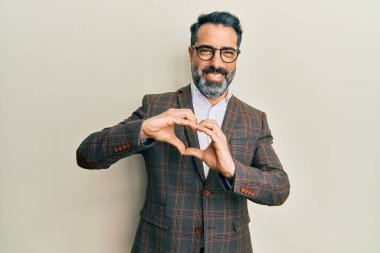 Orta yaşlı, sakallı, gri saçlı, iş ceketi giyen, gözlüklü, aşkla gülümseyen, elleriyle kalp sembolü yapan bir adam. romantik kavram. 