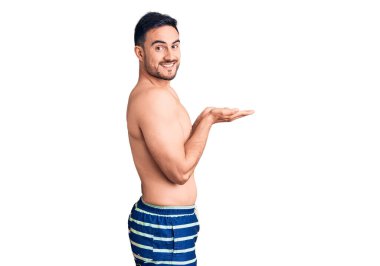 Mayo giyen genç yakışıklı adam avuçlarını açıp fotokopi alanını gösteriyor, gülümseyerek mutlu bir şekilde gülümsüyor. 