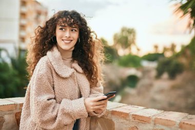 Genç İspanyol kadın şehirde akıllı telefon kullanarak mutlu bir şekilde gülümsüyor.