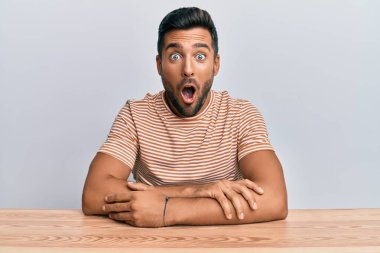 Yakışıklı İspanyol bir adam, gündelik giysiler giymiş masada korkmuş ve şok olmuş bir şekilde oturuyor.. 