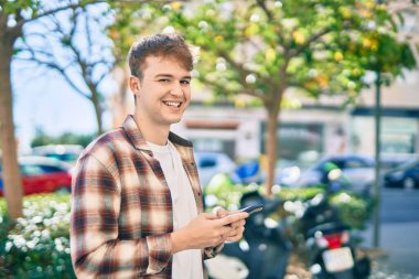 Beyaz adam şehirde akıllı telefon kullanarak mutlu bir şekilde gülümsüyor..