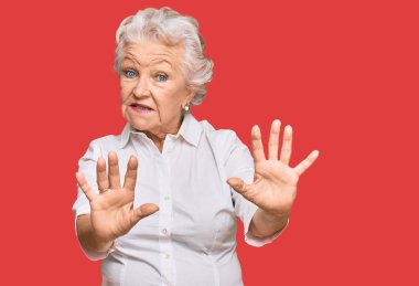 Yaşlı, gri saçlı, günlük kıyafetler giyen, korku ifadesinden korkan, dehşete düşmüş, elleriyle hareket etmeyi kesen, şok içinde bağıran bir kadın. panik konsepti. 
