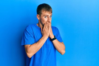 Günlük mavi tişört giyen genç beyaz adam gülüyor ve utanıyor kıkırdıyor ağzı ellerle, dedikoduyla ve skandal konseptiyle örtüyor. 