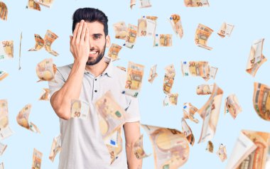 Sakallı, sıradan polo giyen, bir gözünü eliyle kapatan, yüzünde kendine güvenen bir gülümseme ve sürpriz bir duygu olan yakışıklı bir adam..