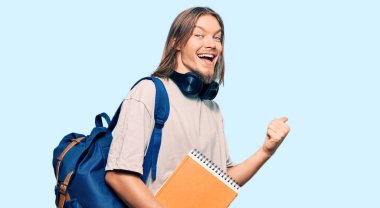 Uzun saçlı, yakışıklı beyaz bir adam. Sırt çantası takıyor ve kitapları tutuyor. Başparmağını kaldırıp gülümsüyor. 