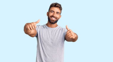 Latin asıllı genç adam gündelik giysiler giyip olumlu jestler yapıyor. Elleriyle gülümsüyor ve başarı için seviniyor. kazanan jest. 