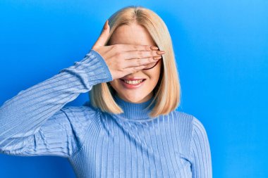 Gündelik kıyafetler giyen, gözlüklü, gülümseyen ve gülümseyen genç sarışın kadın şaşırtmak için gözlerini kapatıyor. kör kavram. 