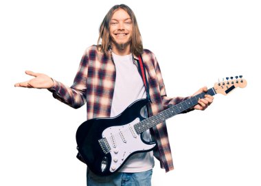 Uzun saçlı yakışıklı beyaz adam zaferi kutlamak için elektro gitar çalıyor mutlu bir gülümseme ve ellerini kaldırarak kazanan ifade. 