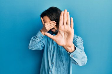 Latin kökenli genç bir adam, günlük kıyafetler giyip, elleriyle gözlerini kapatıyor ve üzgün ve korku ifadeleriyle jestleri durduruyor. utangaç ve olumsuz kavram. 