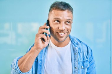 Genç beyaz adam gülümsüyor. Şehirdeki akıllı telefondan konuşuyor..