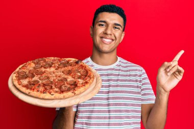 İtalyan pizzası tutan genç bir Arap, mutlu bir şekilde gülümsüyor. 