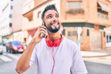 Genç Arap adam gülümsüyor. Akıllı telefonla konuşuyor ve şehirde kulaklık takıyor..