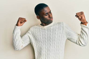 Sıradan kıyafetler giyen genç Afrikalı Amerikalı gururla gülümseyen kol kaslarını gösteriyor. fitness konsepti. 