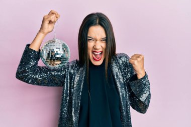 Genç İspanyol kız parlak disko topunu tutuyor gururla bağırıyor, zaferi kutluyor ve başarıyı kollarını kaldırarak kutluyor. 
