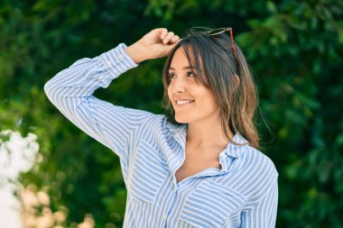 Genç İspanyol kadın gülümsüyor. Parkta güneş gözlüğüne dokunduğu için mutlu..