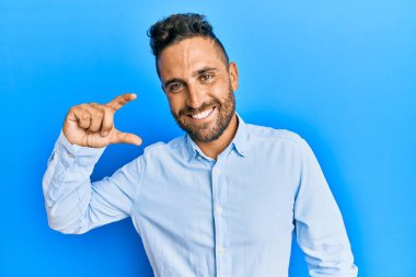 Sakallı, sıradan giyinen, gülümseyen, kendine güvenen, el hareketleriyle hareket eden, parmaklarıyla işaret eden ve kameraya bakan yakışıklı bir adam. ölçüm kavramı. 