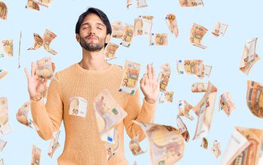 Yakışıklı İspanyol kazak giyen rahat ve gözleri kapalı gülümseyen parmaklarıyla meditasyon hareketi yapan adam. yoga konsepti.