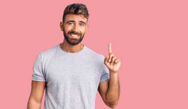 Gündelik kıyafetler giyen genç İspanyol bir numarayı gösterip işaret ederken kendinden emin ve mutlu bir şekilde gülümsüyor.. 