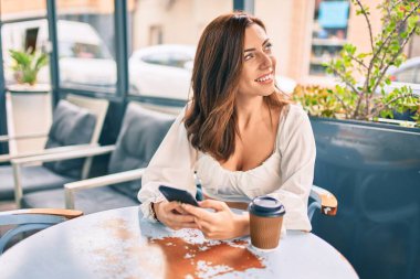 Genç İspanyol kadın kahvehanenin terasında akıllı telefon kullanarak mutlu gülümsüyor..