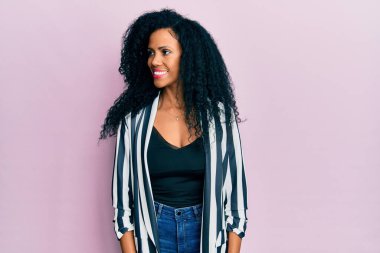 Orta yaşlı Afro-Amerikalı kadın, günlük kıyafetler giyip yüzünde gülümseme, doğal bir ifade ile yan yana bakıyor. Kendinden emin gülen. 