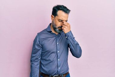 Orta yaşlı, sakallı, gri saçlı, iş kıyafetleri giyen, burnu ve gözleri ovuşturan, yorgunluk ve baş ağrısı çeken bir adam. Stres ve hüsran kavramı. 