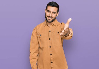 Gündelik kıyafetler giyen genç İspanyol adam dostça bir selamlama ve hoş geldin hediyesi olarak el sıkışmayı sunuyor. başarılı iş. 