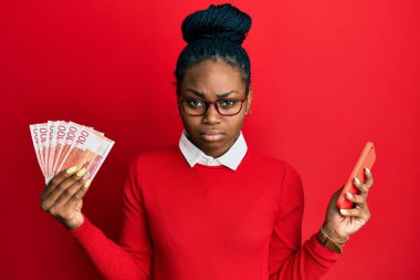 Genç Afro-Amerikalı kadın elinde Norveç Kronu ile akıllı telefon kullanıyor şüpheci ve sinirli, sorun yüzünden üzgün. negatif kişi. 