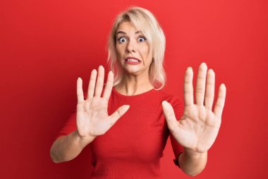 Sıradan kıyafetler giyen genç sarışın kız korku ifadesinden korkuyor ve dehşete düşüyor. El hareketlerini durdur, şok içinde bağır. panik konsepti. 