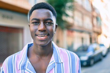 Genç Afro-Amerikan adam gülümsüyor. Şehrin caddesinde mutlu bir şekilde duruyor..