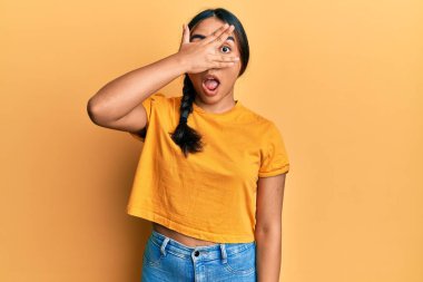 Gündelik kıyafetler giyen genç Latin kadın şok içinde yüzünü ve gözlerini kapayarak utanmış ifadesiyle parmaklarından bakıyor.. 