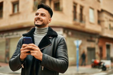 Genç Arap adam şehirde akıllı telefon kullanarak mutlu gülümsüyor..