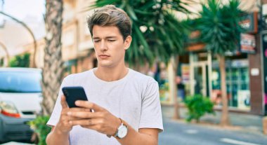 Şehirde akıllı telefon kullanan, ciddi bir suratı olan beyaz bir genç..