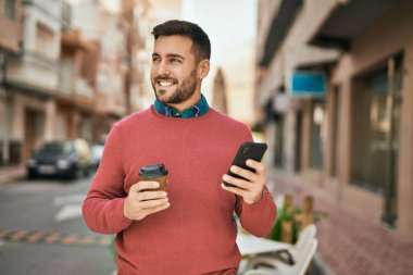 Genç İspanyol adam akıllı telefon kullanıyor ve şehirde kahve içiyor..