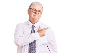 Yaşlı, gri saçlı, iş kıyafetleri giyen, neşeli, yüzünde mutlu ve doğal bir ifadeyle el ve parmak uçlarını gösteren bir gülümseme olan adam. 