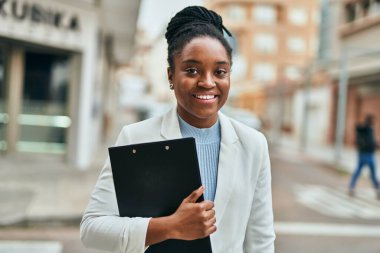 Genç Afrikalı Amerikalı iş kadını, şehirde elinde bir panoyla mutlu bir şekilde gülümsüyor..
