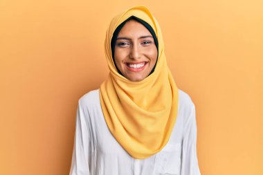 Genç esmer Arap kadın geleneksel İslami başörtüsü takıyor ve yüzünde mutlu ve havalı bir gülümseme var. şanslı kişi. 