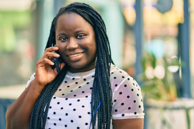 Genç Afrikalı Amerikalı kadın gülümsüyor. Şehirdeki akıllı telefondan mutlu bir şekilde konuşuyor..