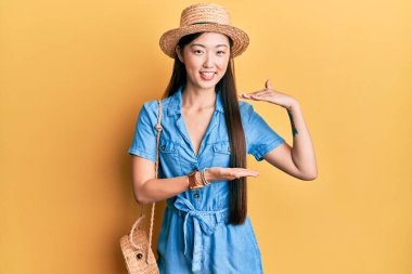 Yazlık şapka takan genç Çinli kadın. Elleriyle işaret ediyor. Büyük ve büyük beden işareti, ölçü sembolü. Kameraya bakıp gülümsüyor. ölçüm kavramı. 