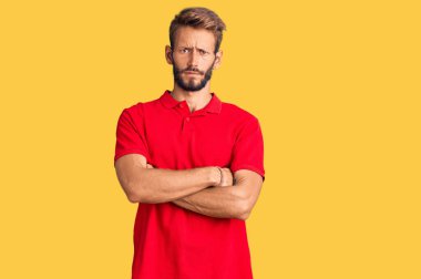 Sarışın, sakallı, sıradan giyinen, kuşkucu ve gergin, yüzünde çapraz kollu bir ifade olan yakışıklı bir adam. negatif kişi. 