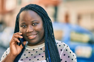 Genç Afrikalı Amerikalı kadın gülümsüyor. Şehirdeki akıllı telefondan mutlu bir şekilde konuşuyor..