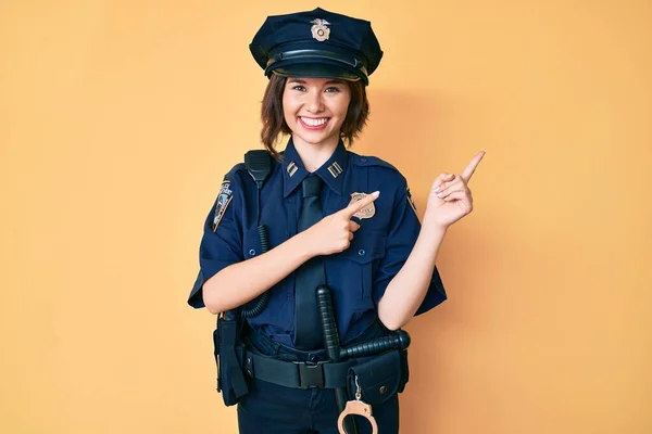 Young beautiful woman wearing police uniform smiling and looking at the camera pointing with two hands and fingers to the side.