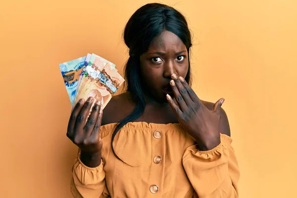 Africká Mladá Žena Držící Kanadské Dolary Ústa Rukou Šokovaná Vystrašená — Stock fotografie