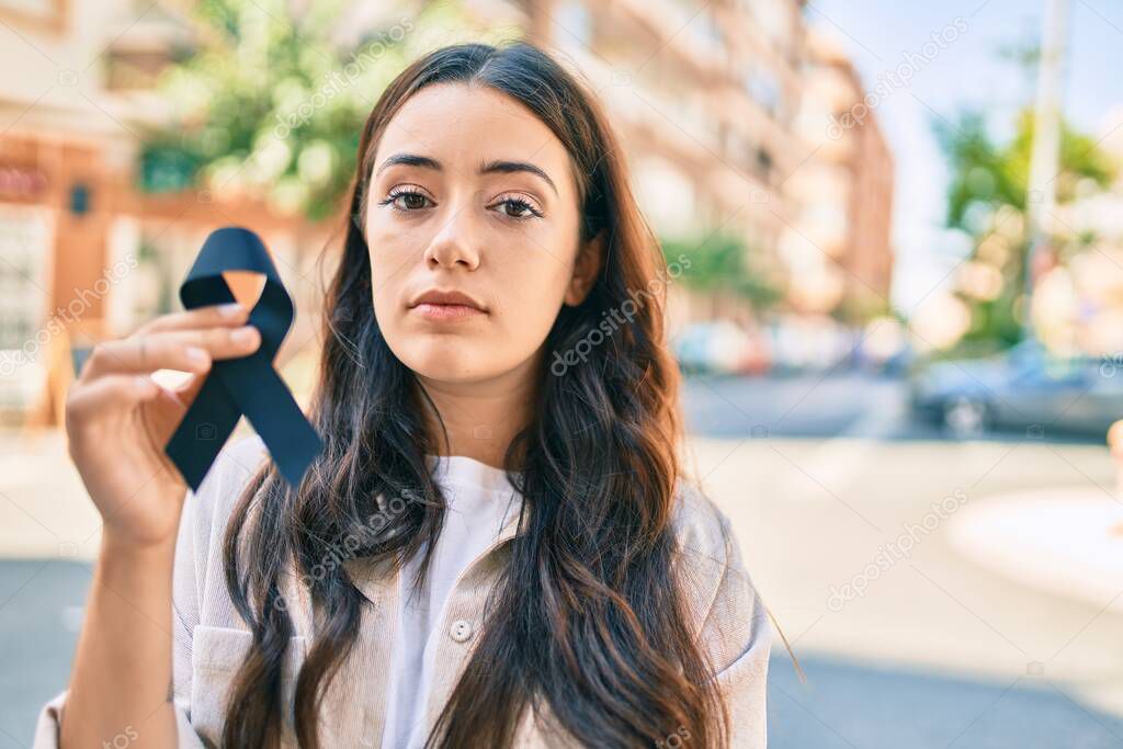 Young hispanic woman with serious expression holding black ribbon at the city.